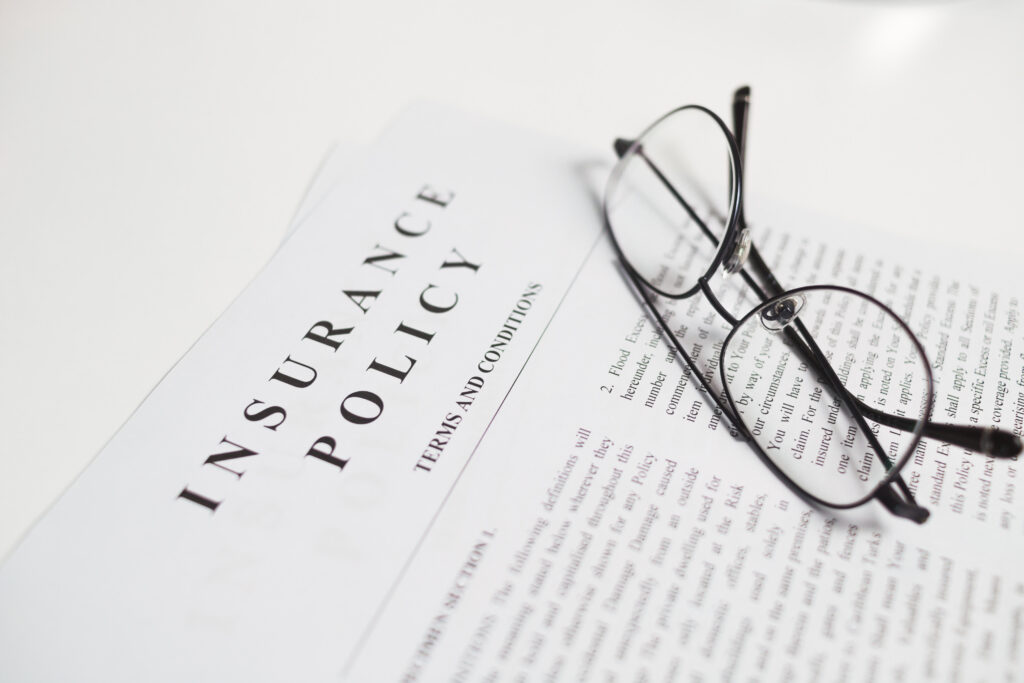 insurance policy contract with spectacles on white table. close up view